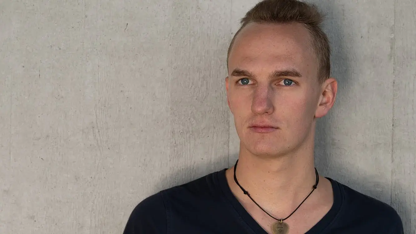 Ein Portrait des Künstlers Frederic Levi in schwarzem Oberteil vor marmoriertem hellgrauen Hintergrund