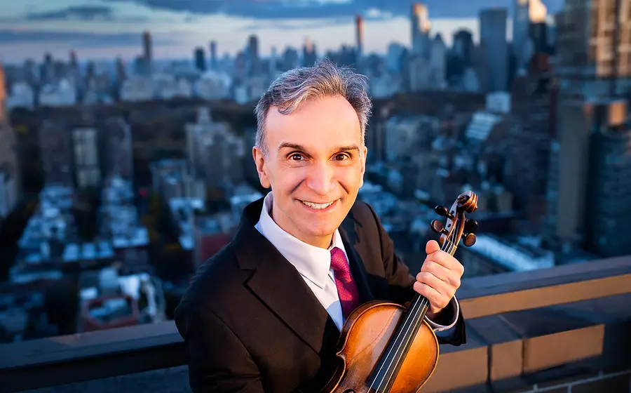 Pressefoto des Violinisten Gil Shaham mit Violine vor Stadtpanorama.