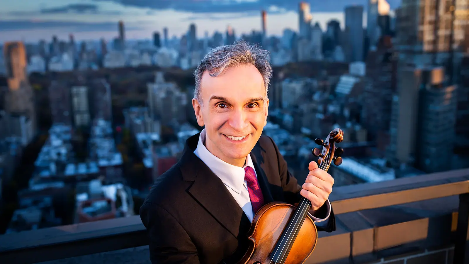 Pressefoto des Violinisten Gil Shaham mit Violine vor Stadtpanorama.
