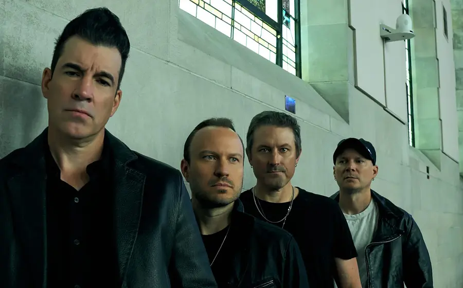Die vier Mitglieder der Band Theory of a dead man stehen an einer Wand gelehnt, oben große Fenster