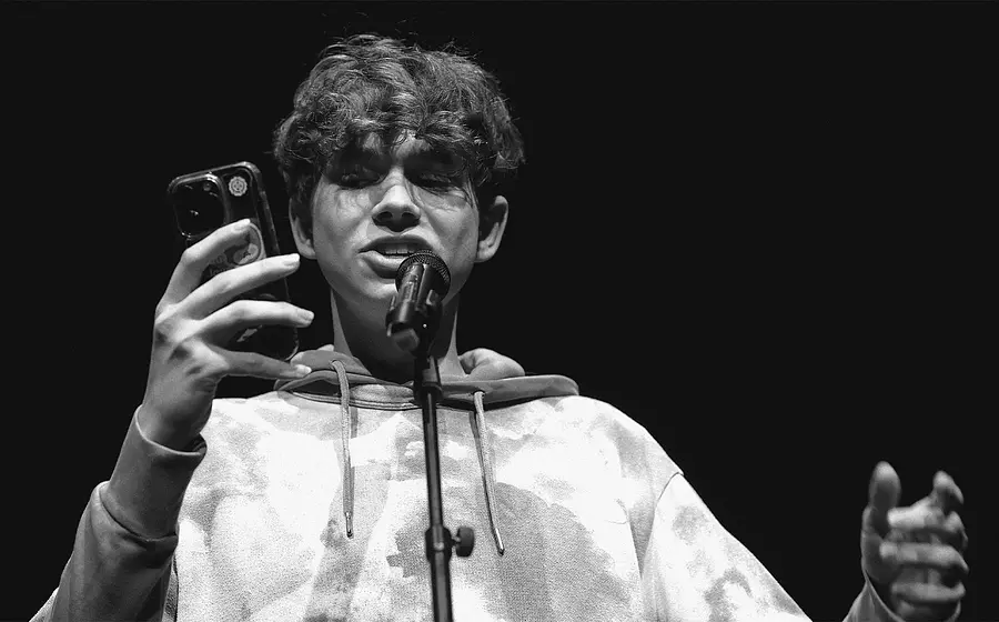 Foto für das Event „U20 POETRY SLAM“ in Schwarz-Weiß, mit einem Jungen, der mit Mikrofon und Handy performt.