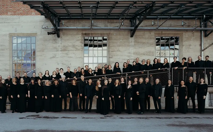 Großes Gruppenfoto des Münchener Bach Chors. Die Mitglieder tragen schwarze Konzertkleidung und sind auf mehreren Ebenen entlang einer Rampe und vor dem Gebäude aufgestellt.