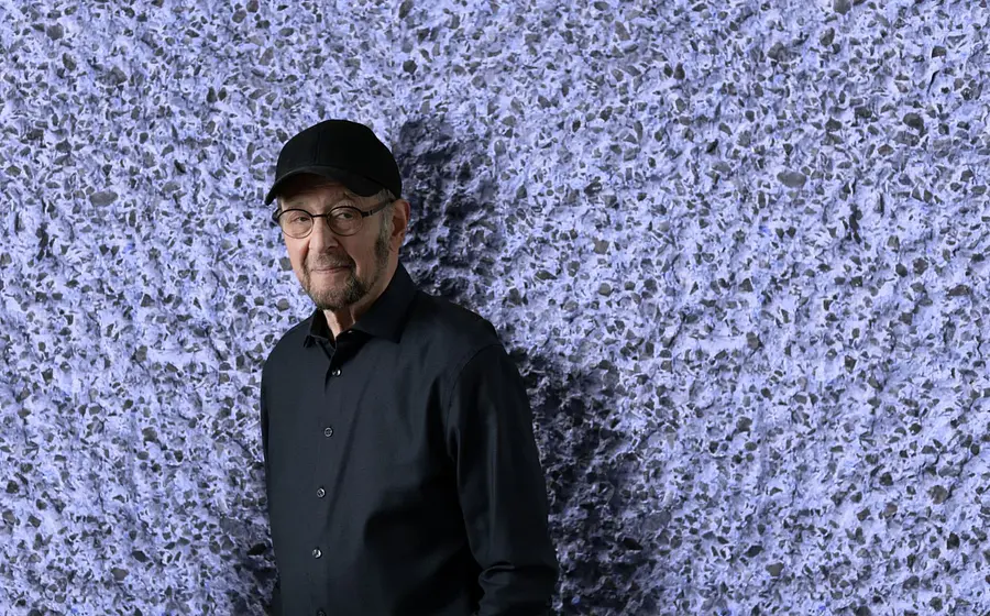 Eine Person in schwarzem Hemd und schwarzer Kappe vor violetter rauher Steinwand zur Veranstaltung KOMPONISTENPORTRÄT STEVE REICH