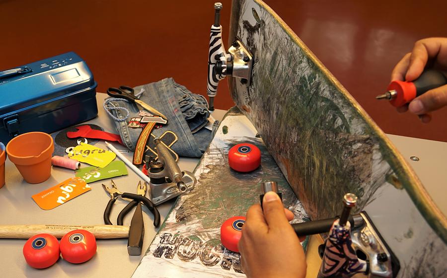 Auf einem Tisch liegen ein kaputtes Skateboard, kaputte Blumentöpfe und eine kaputte Jeans und die Hilfsmittel, um sie zu reparieren.