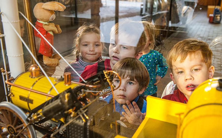Fünf Kinder gucken in eine Vitrine, in der sich das Modell einer gelben Lokomotive befindet. Auf der linken Seite ist eine Hasen-Stoffpuppe zu sehen.